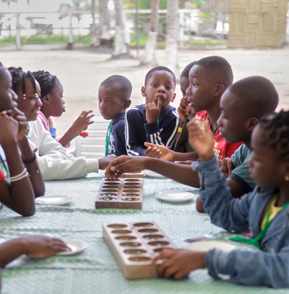 Des enfants jouent à l'awalé autour d'une table, au camp Mi-Adja 2025 à San Pedro